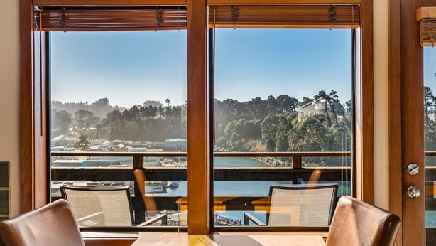 A dining area with a table and chairs, large windows with a view of a coastal landscape and buildings. - Harbor Lite Lodge (Fort Bragg)