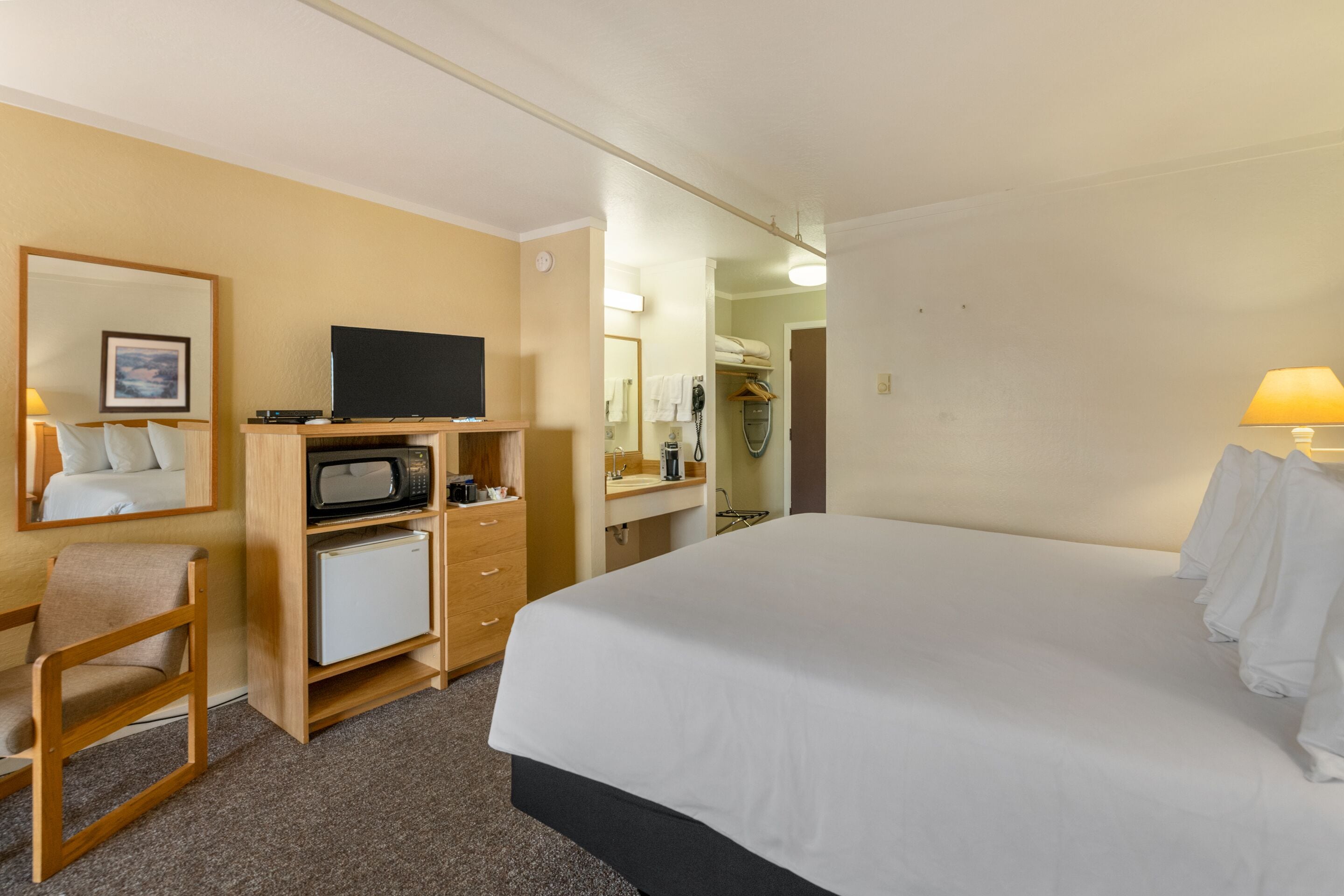 Una camera d'albergo con un letto, una scrivania con televisore, un forno a microonde e un piccolo frigorifero.