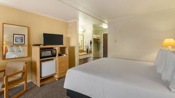A hotel room with a bed, a desk with a TV, a microwave, and a small refrigerator.