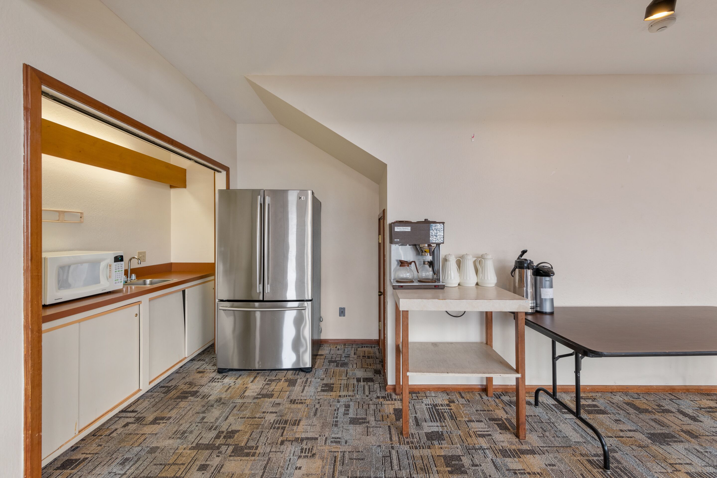 A compact kitchen with a stainless steel refrigerator, a microwave, and a coffee maker on a small table.