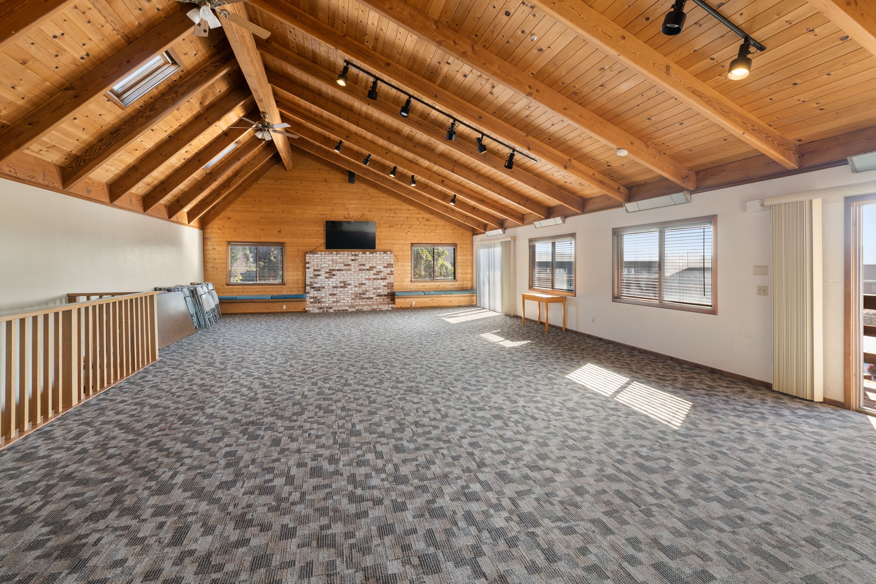 Une pièce spacieuse avec un haut plafond en bois, une cheminée, de grandes fenêtres et un sol recouvert de moquette.