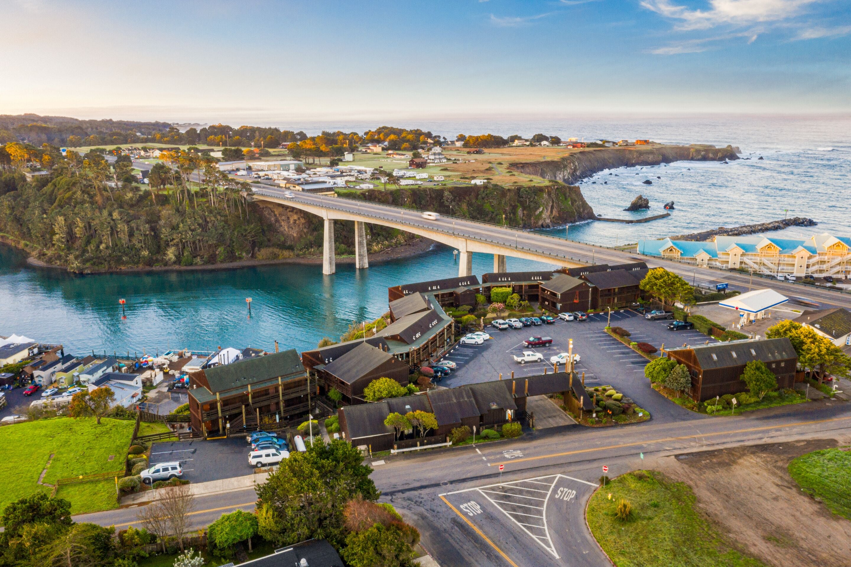 A coastal hotel with a parking lot, a bridge, and a view of the sea.