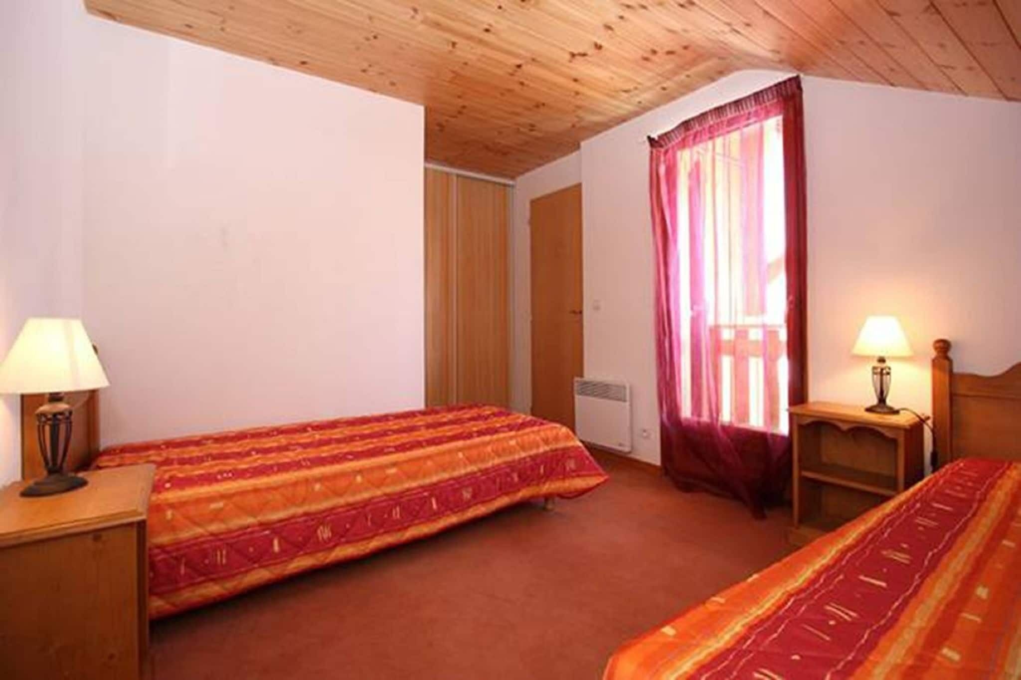 Una habitación con dos camas, techo de madera, ventana con cortinas y lámparas de noche.