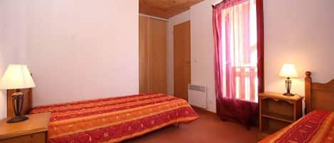 Una habitación con dos camas, techo de madera, ventana con cortinas y lámparas de noche.