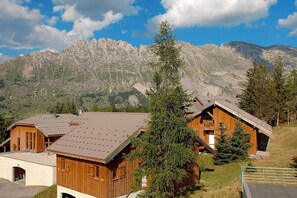 Eine Holzhütte mit geneigtem Dach, eingebettet in eine gebirgige Landschaft.