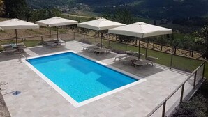 Una piscina con sillas de descanso y sombrillas, rodeada por una valla, y un paisaje montañoso al fondo.