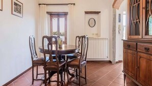 Un comedor con una mesa redonda y cuatro sillas, un armario de madera, una ventana con cortinas y un radiador.