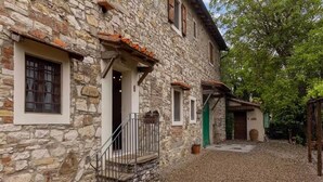 Un edificio de piedra con un patio de grava, una escalera de madera y una puerta verde.