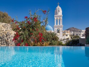 A clear blue swimming pool with a white building and a clock tower in the background. - Villa in Megalochori with Private Pool (Megalochori)