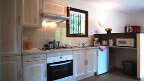Une cuisine compacte avec des meubles en bois, un four encastré, un four à micro-ondes et une fenêtre donnant sur un espace verdoyant.