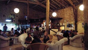 Un intérieur rustique avec des murs en pierre et des poutres en bois, agrémenté de meubles en osier et d’un coin bar.