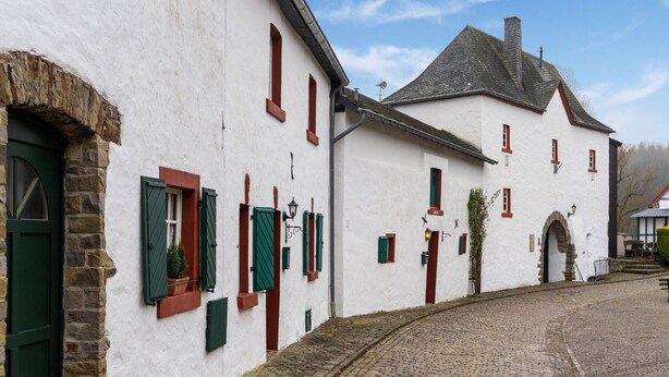 En traditionell byggnad med en kullerstensgata, en entré med en valvformad stenöppning och en liten trädgård.
