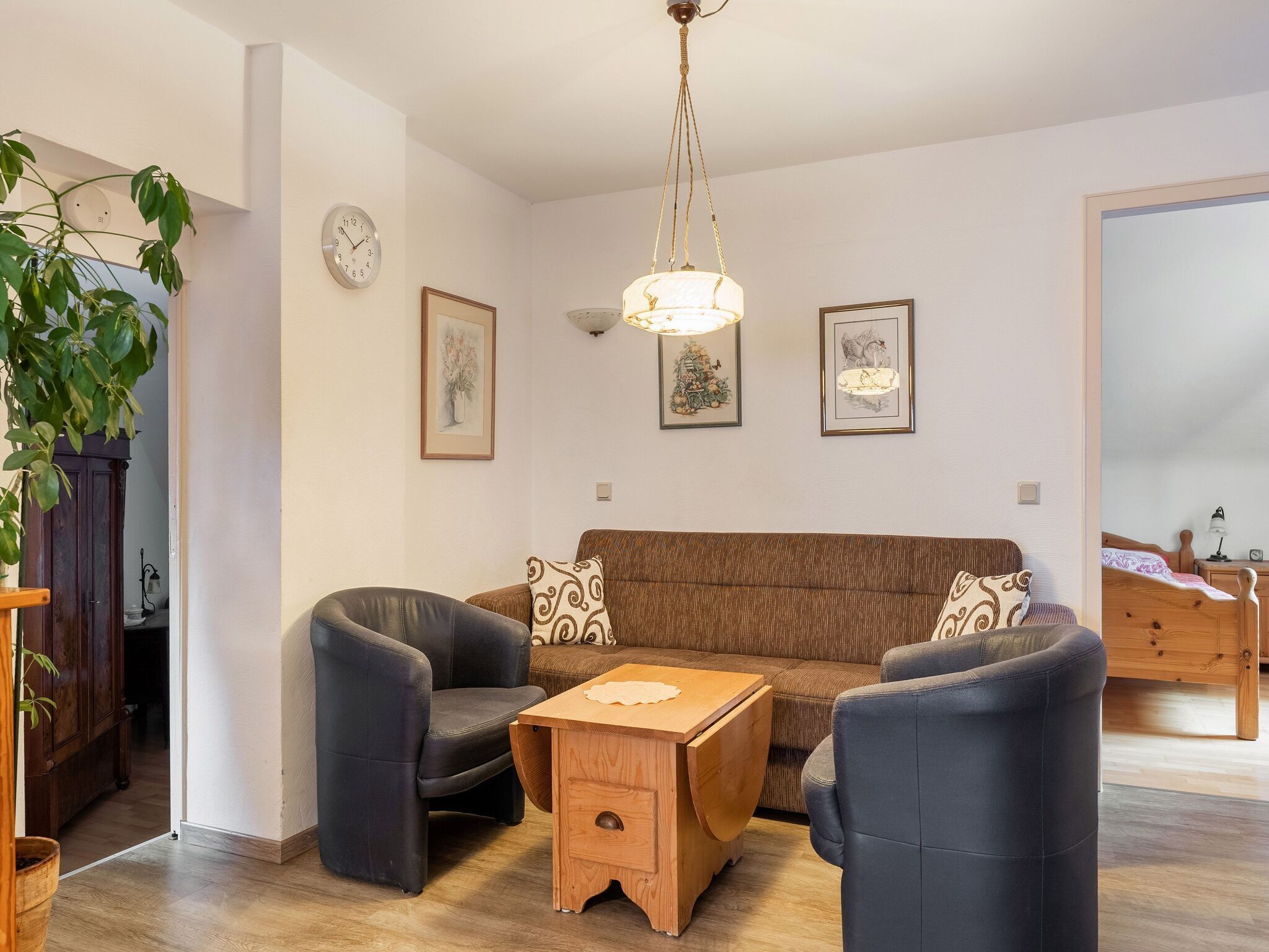 Un salon avec un canapé marron, deux fauteuils noirs, une table basse en bois et un luminaire suspendu.