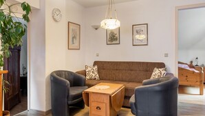 Ett vardagsrum med en brun soffa, två svarta fåtöljer, ett träbord och en hängande lampa.