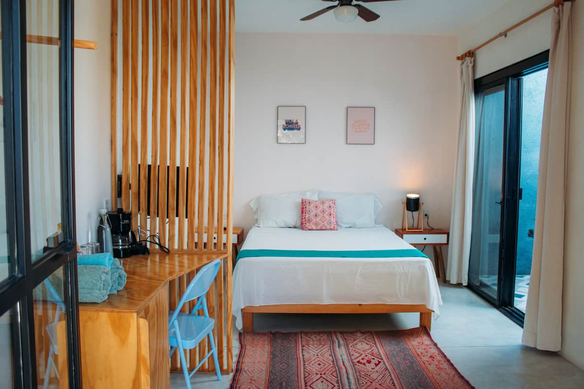 A bedroom with a bed, a desk, a chair, and a view of the sea through a sliding door.