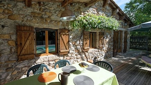 Un espace de restauration en plein air agrémenté d’un mur en pierre, de volets en bois et d’une table dressée pour deux personnes.