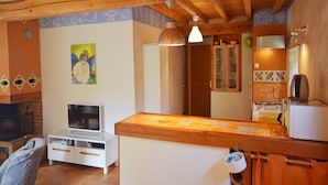 Un salon confortable avec un téléviseur, des meubles en bois, un tableau et un coin cuisine équipé d’un évier et de placards.