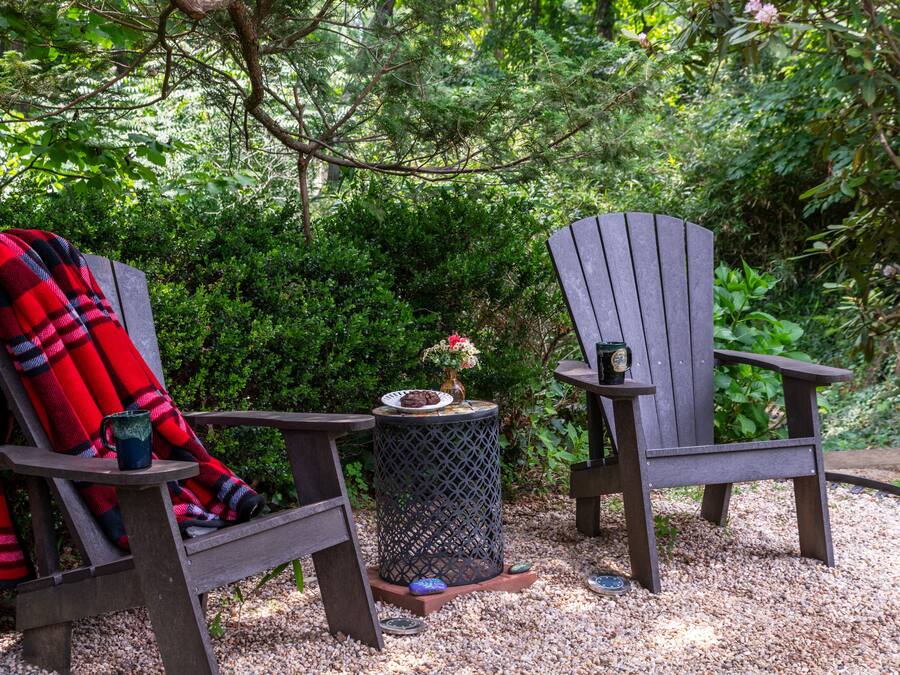 Twee Adirondack stoelen met een ruitendeken en een bijzettafeltje met een vaas en een mok ertussen.