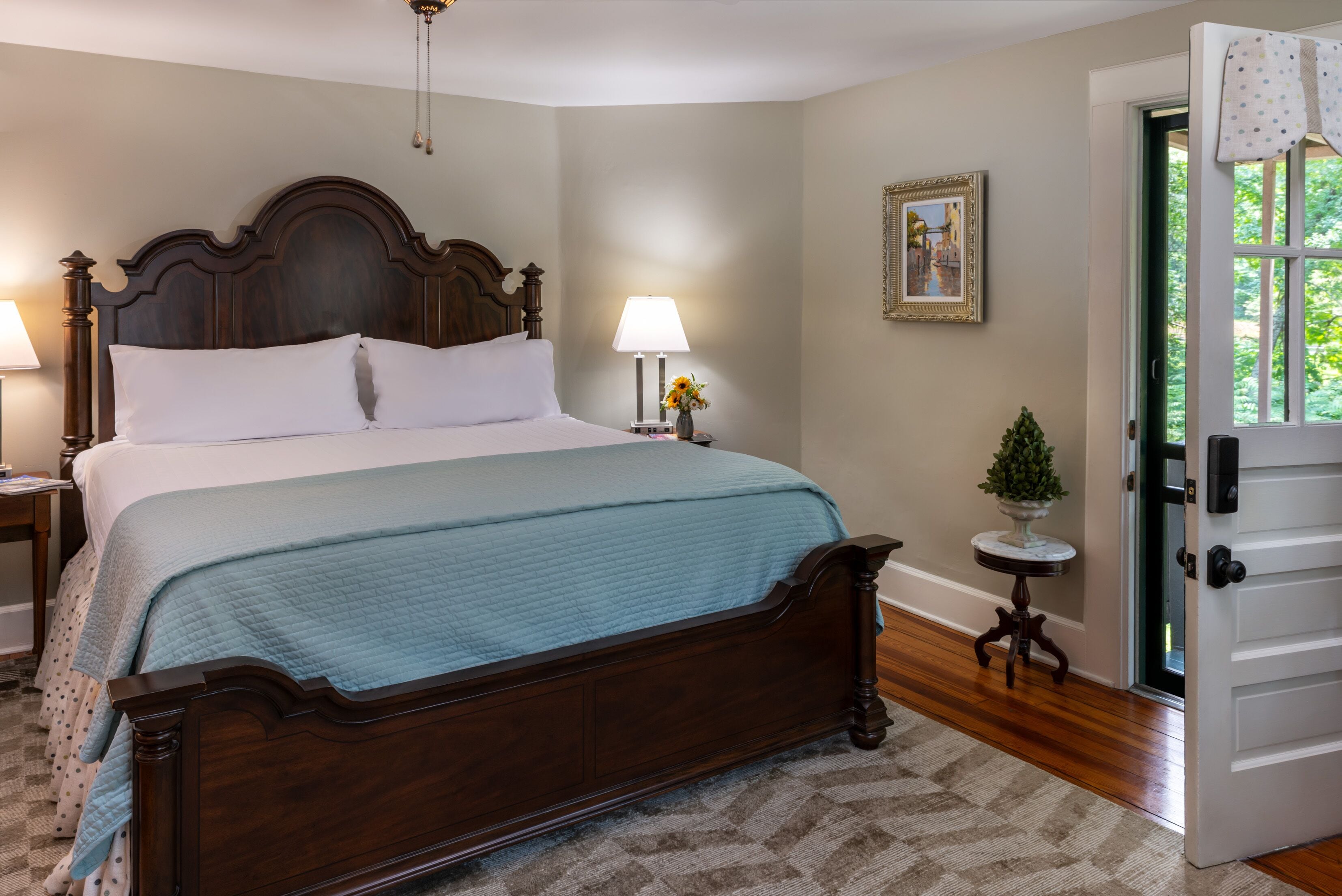 A neatly made bed with a wooden headboard, a bedside lamp, and a small table with a vase of flowers.