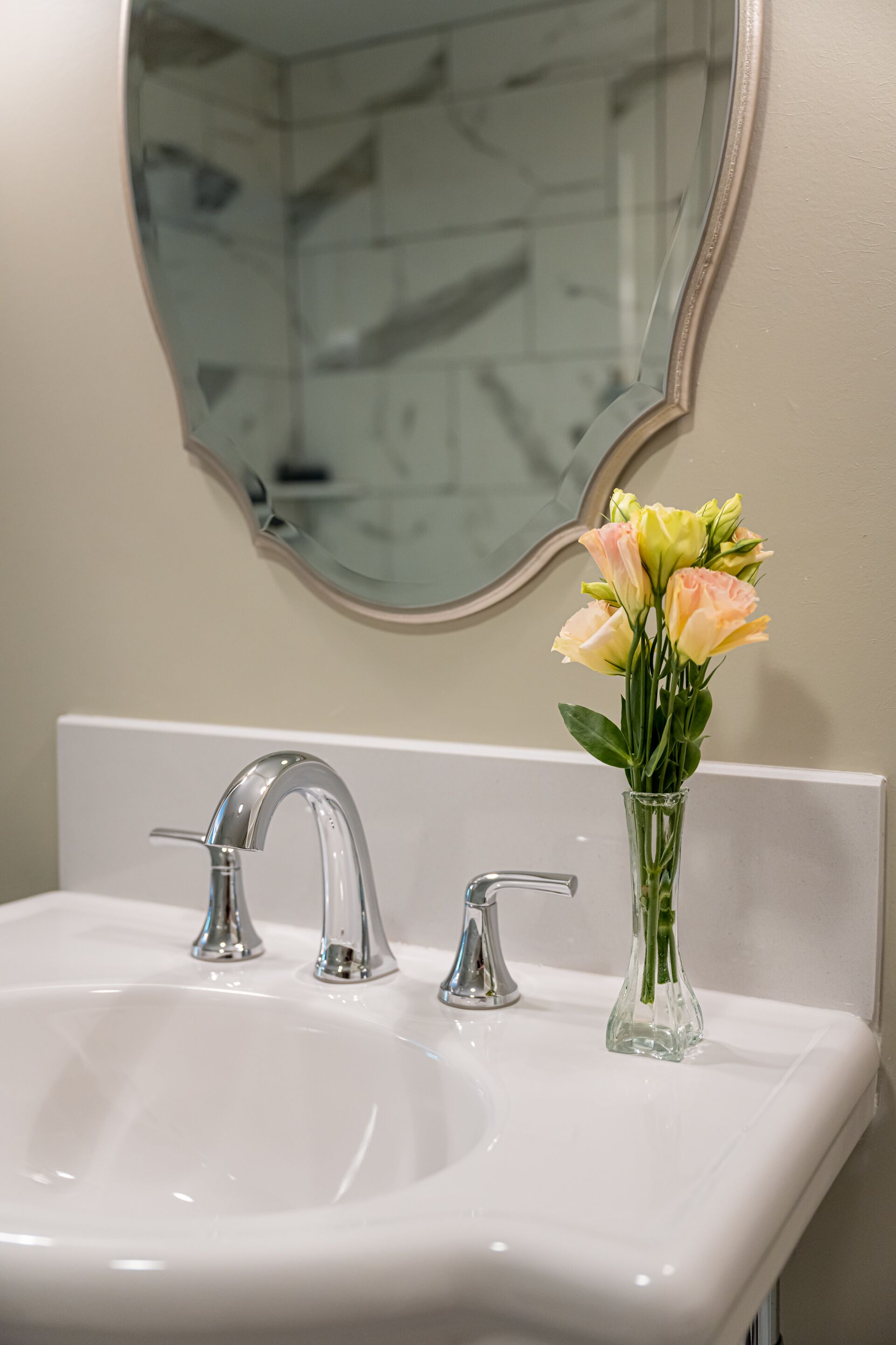 A bathroom sink with two faucets and a vase of flowers.
