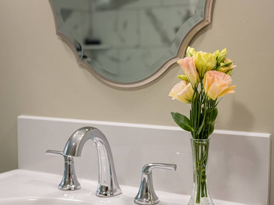 A bathroom sink with two faucets and a vase of flowers.