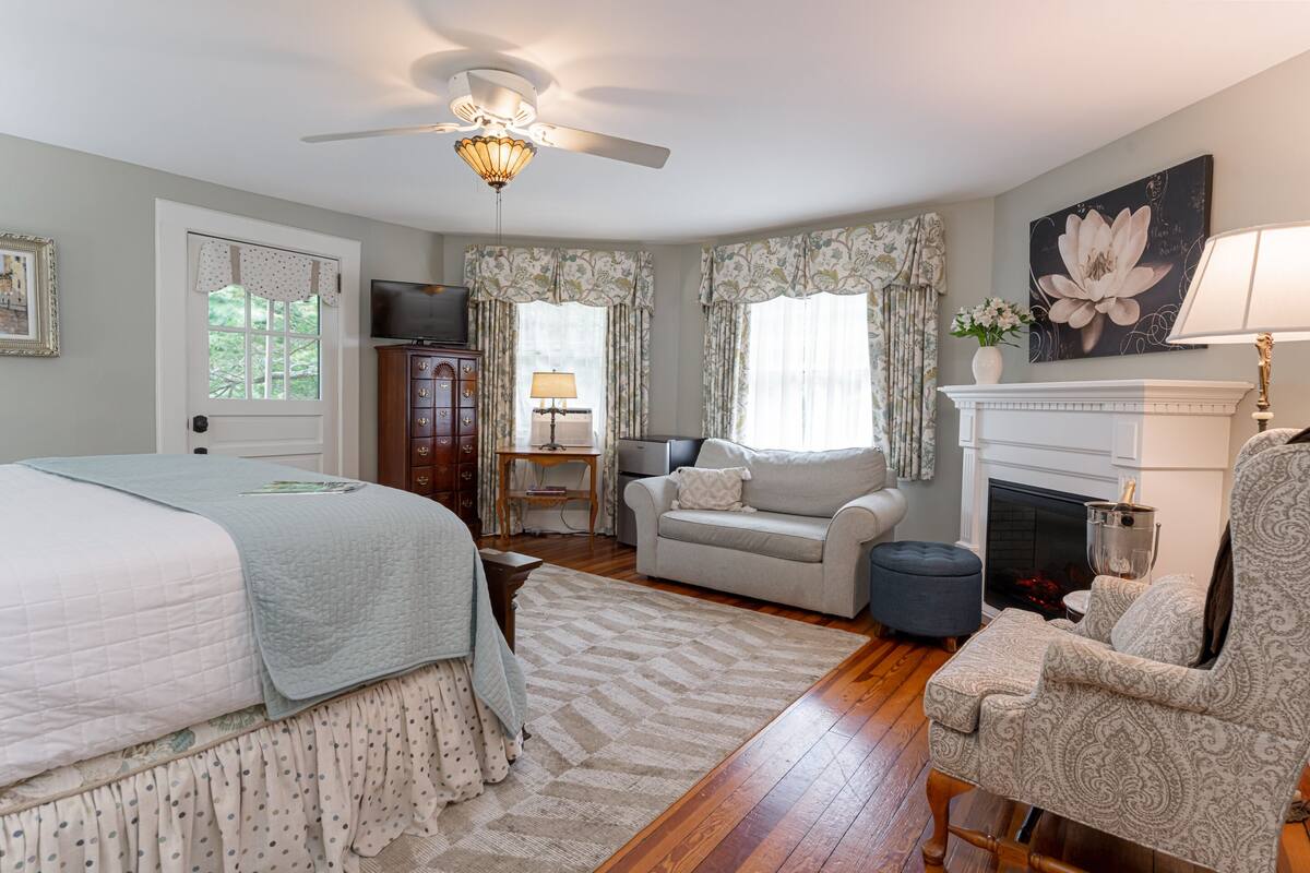 A bedroom with a bed, a dresser, a television, a fireplace, and a ceiling fan.