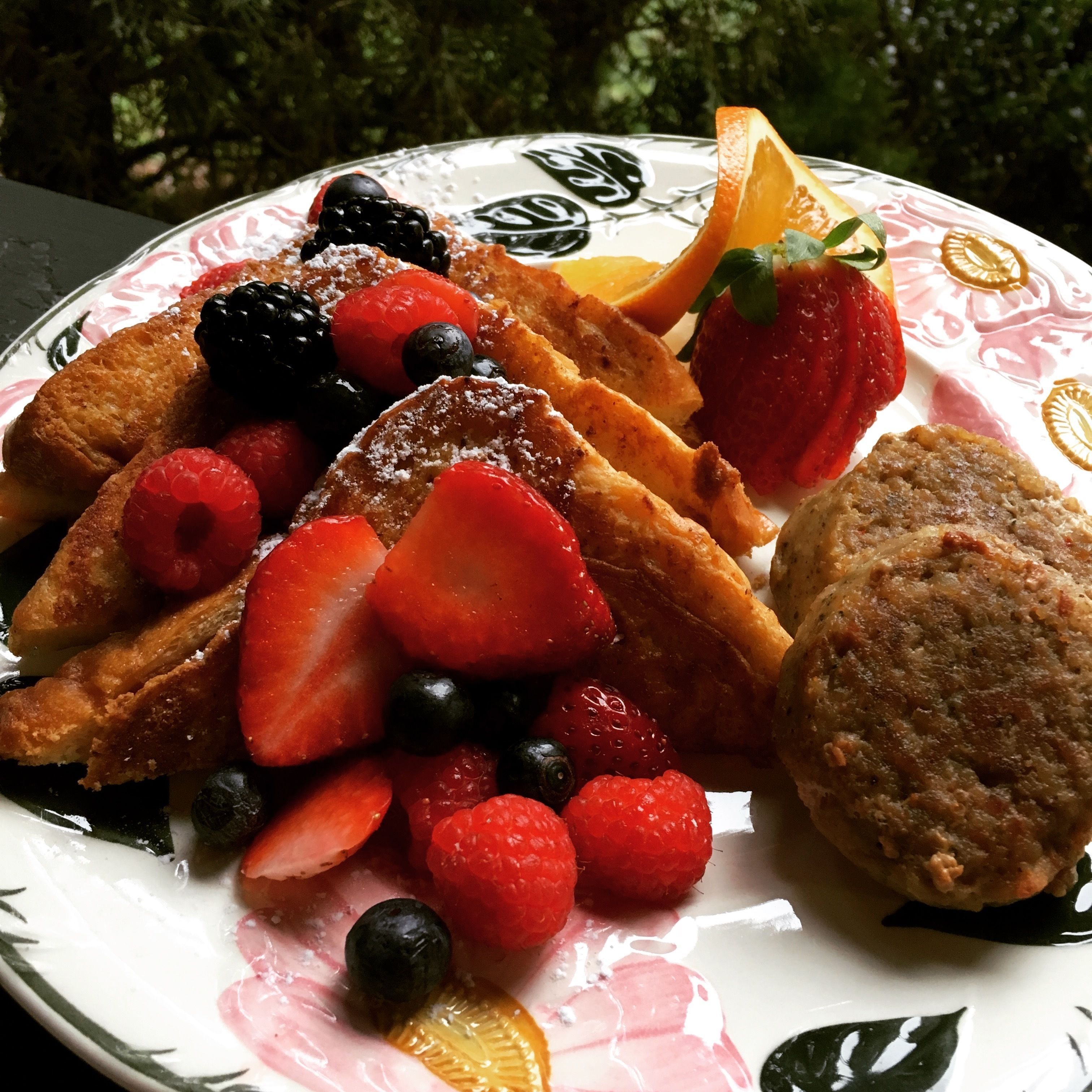 A plate with French toast, strawberries, blueberries, raspberries, and a muffin.