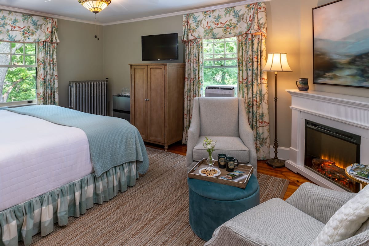A bedroom with two beds, a sitting area with a fireplace, and a television on the wall.