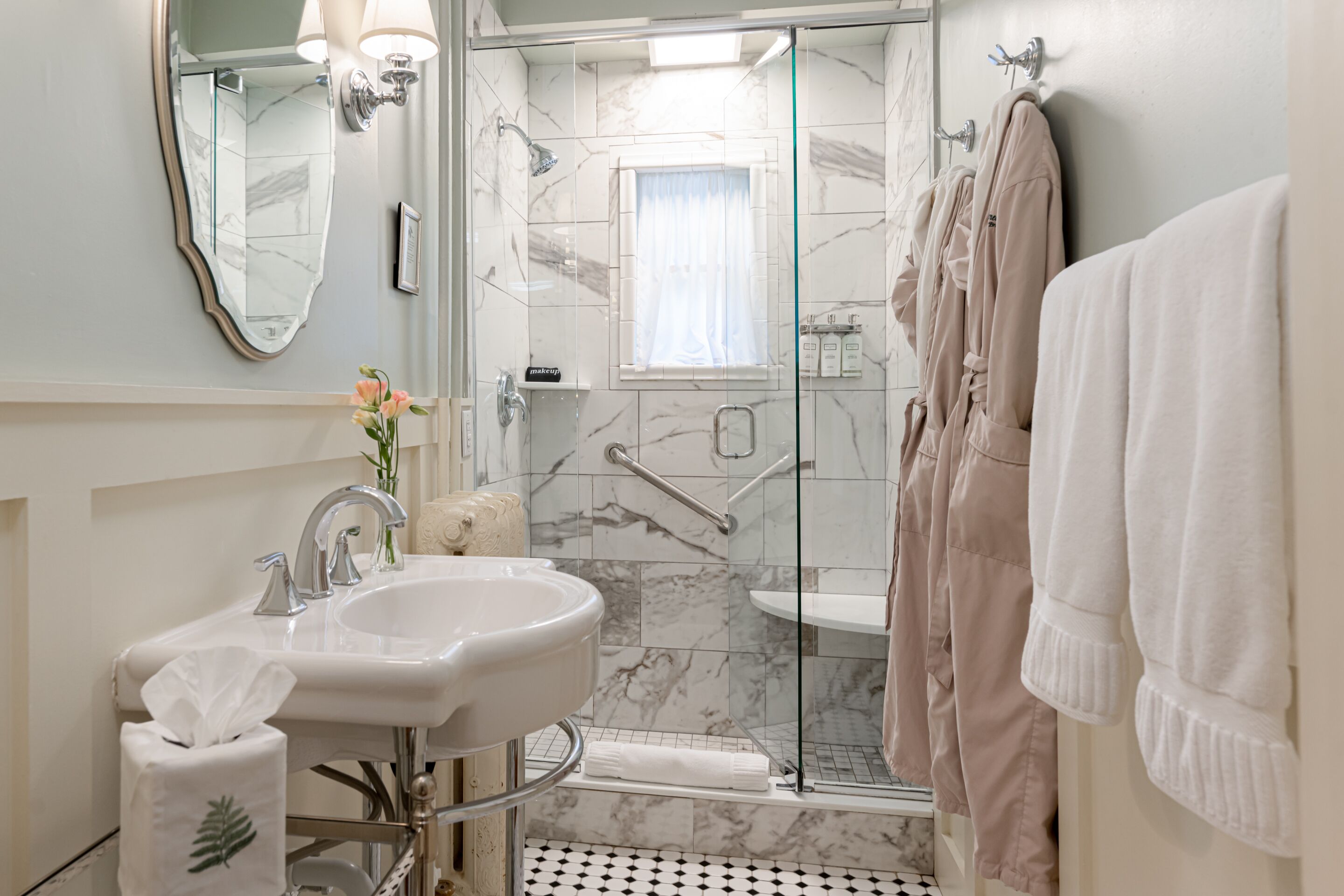 A bathroom with a marble sink, a glass shower enclosure, and a towel rack with towels.