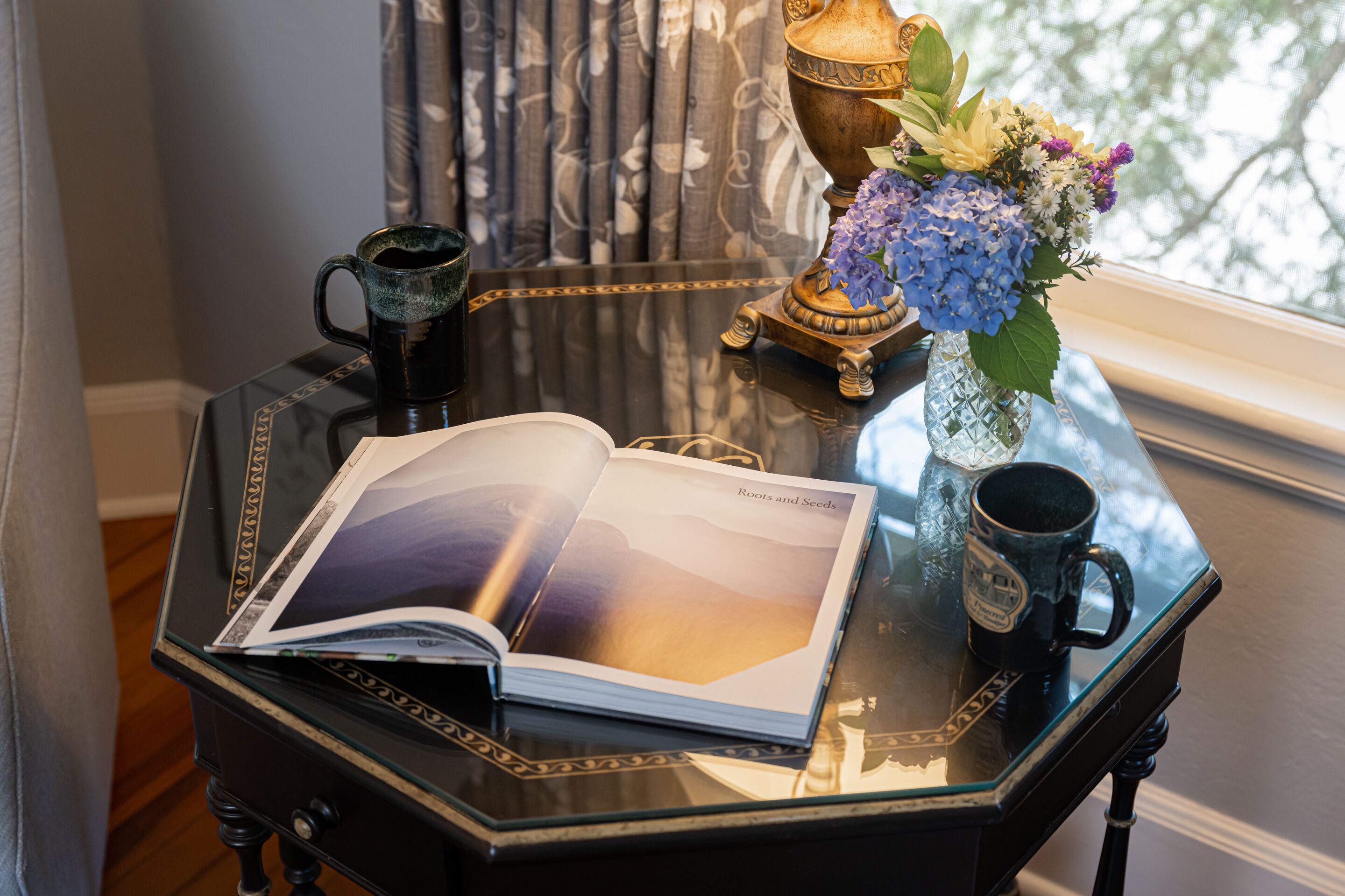 Una mesa con un libro, una taza y un florero con flores.