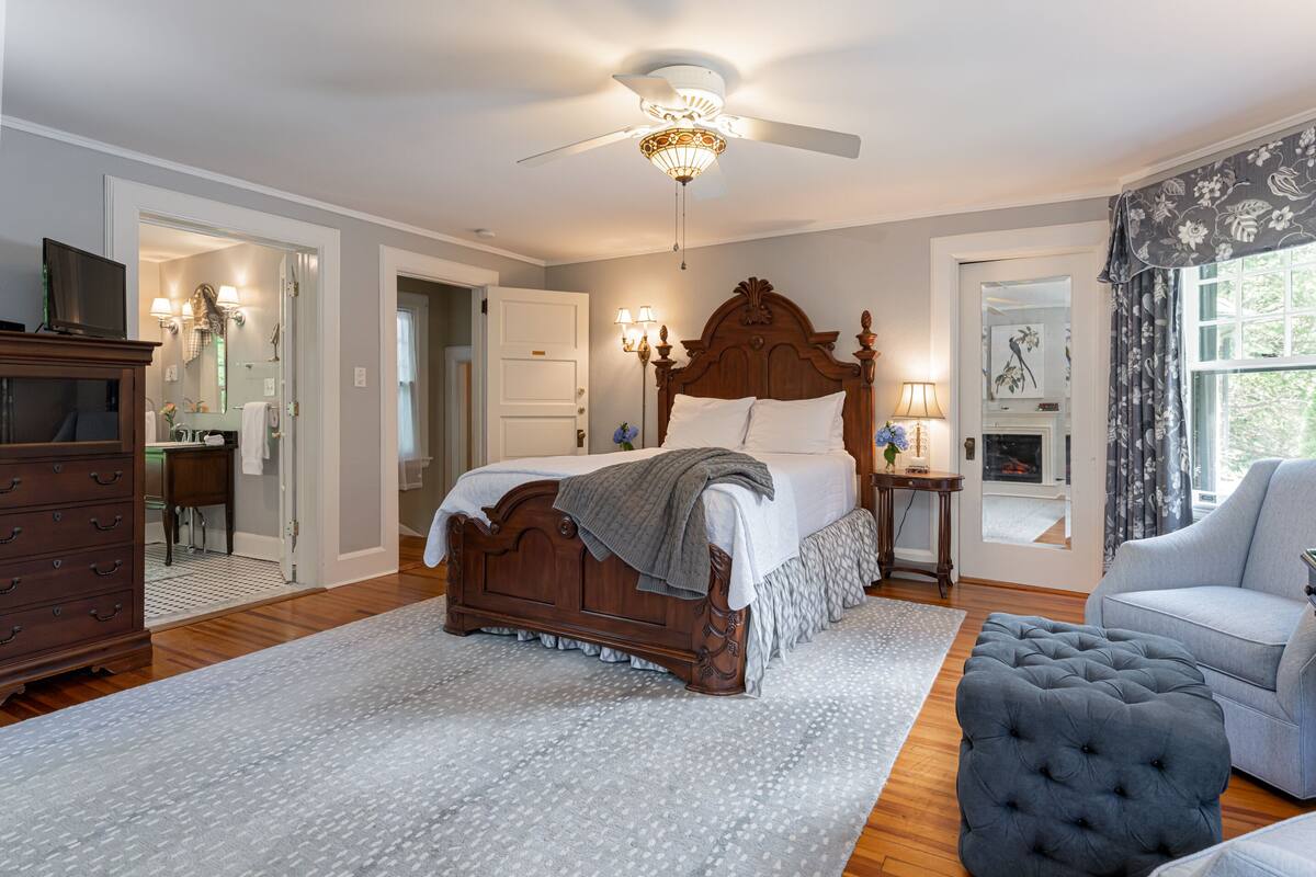 A bedroom with a wooden bed, a ceiling fan, a nightstand, a lamp, a chair, and a dresser.