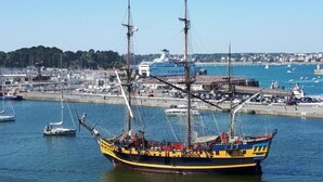 Un gran vaixell veler amarrat al port, amb un paisatge urbà al fons.
