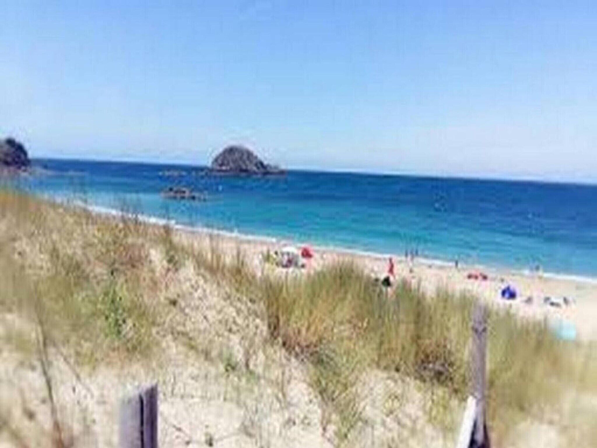 Una playa con cielos despejados, una orilla arenosa y una pequeña isla en la distancia.