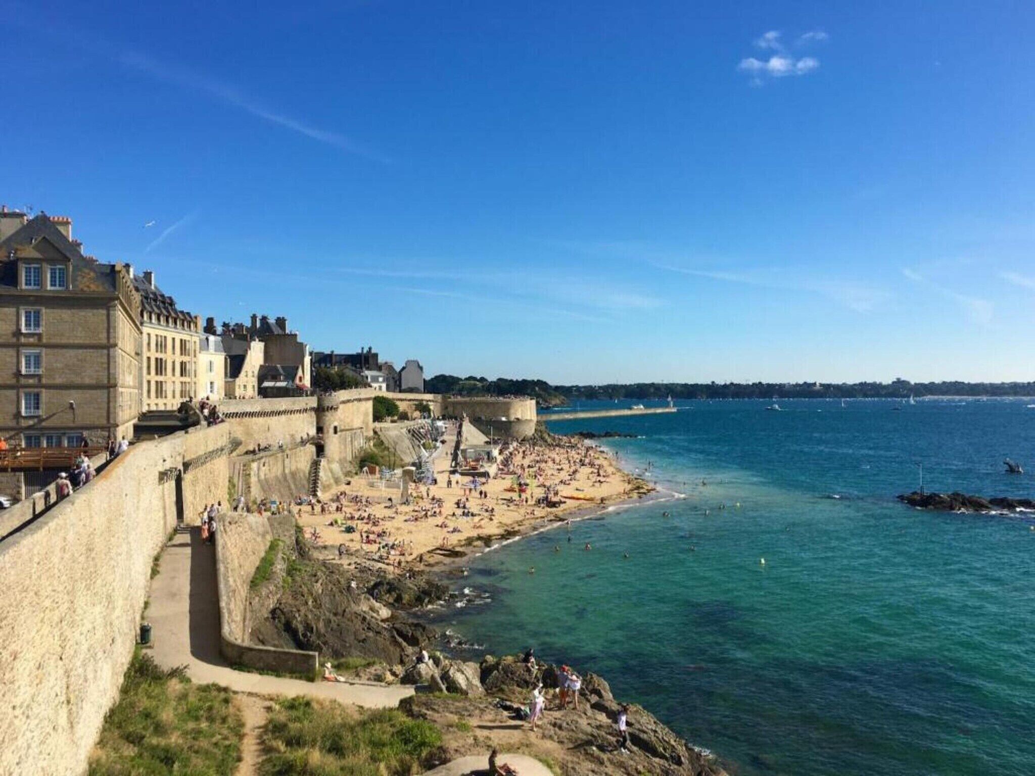 Eine Küstenstadt mit einer befestigten Mauer, einem Sandstrand und einem tiefblauen Meer.
