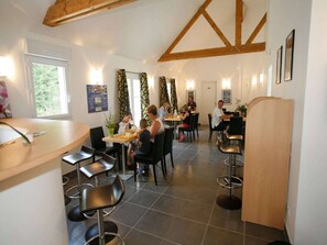 A restaurant with multiple tables and chairs, a wooden ceiling, and a tiled floor. - Apartment in Brittany near Emerald Coast (Le Tronchet)