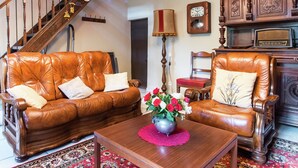 Ein Wohnzimmer mit Holzboden, einer Holztreppe, Ledersofas, einem Couchtisch aus Holz mit Blumenvase und einem Holzschrank mit dekorativen Schnitzereien.