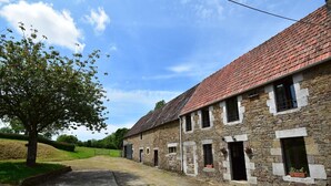 Ein Steinhaus mit rotem Ziegeldach, ein Baum im Vordergrund und ein klarer Himmel.
