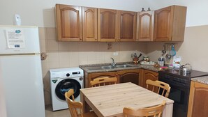 A compact kitchen with wooden cabinets, a washing machine, a sink, and a dining table with chairs. - Holiday Home in Giardini Naxos near Beach (Taormina Messina)