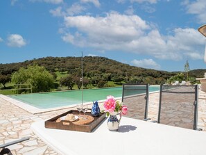 A poolside area with a view of a mountain, a table with a tray of food and drinks, and a vase of flowers. - Farmhouse Dreams: Explore and Relax (Montemor O Novo)