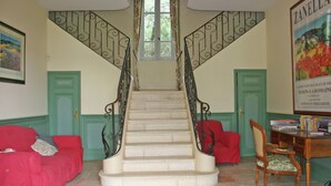 A staircase with ornate metal railings, a green door, and a red sofa in a room with a tiled floor and a framed picture on the wall. - Holiday Home near Mont Ventoux Pool (Vaison-La-Romaine)