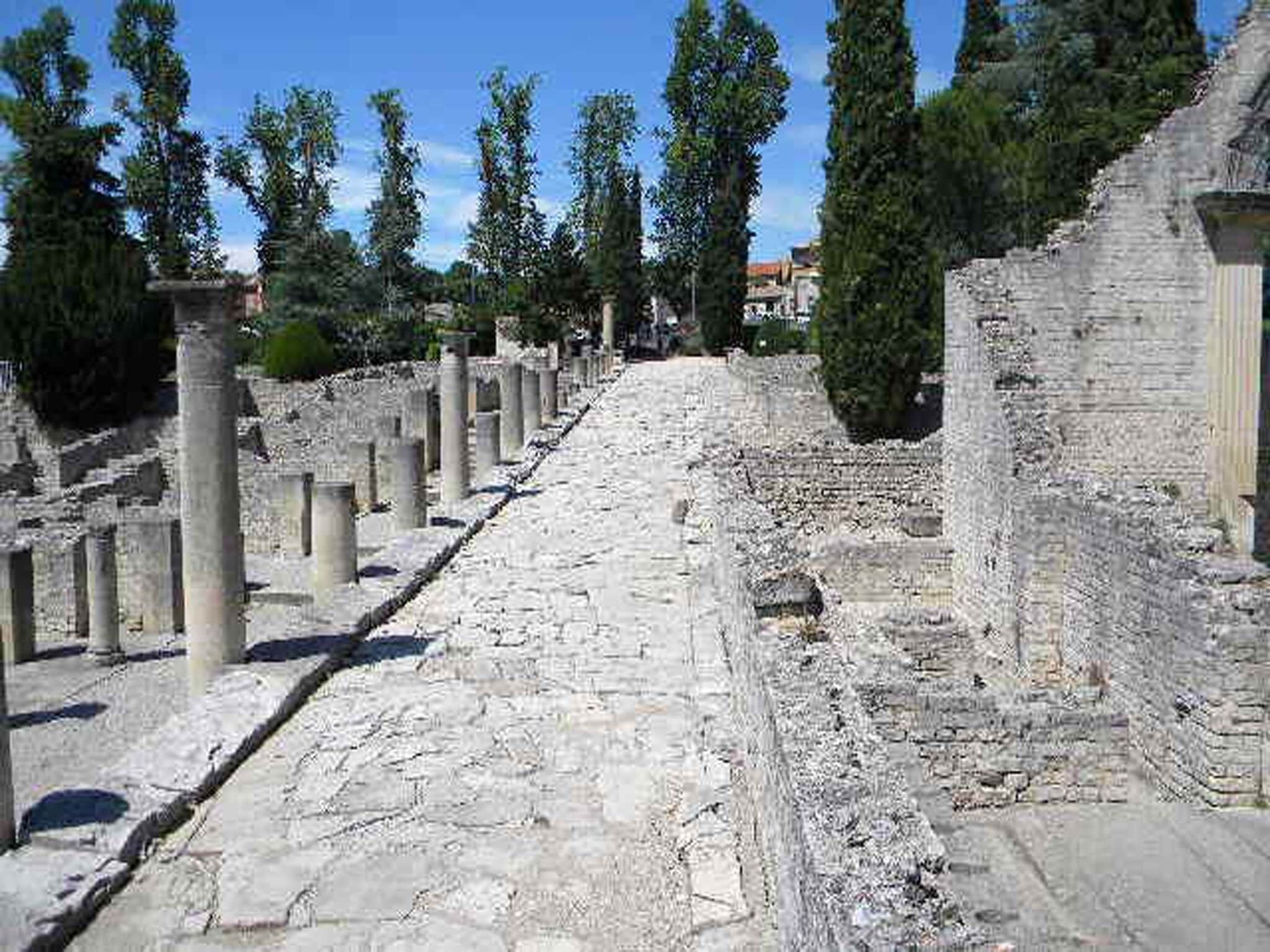 Un sendero de piedra antigua flanqueado por columnas, que conduce a un edificio clásico.