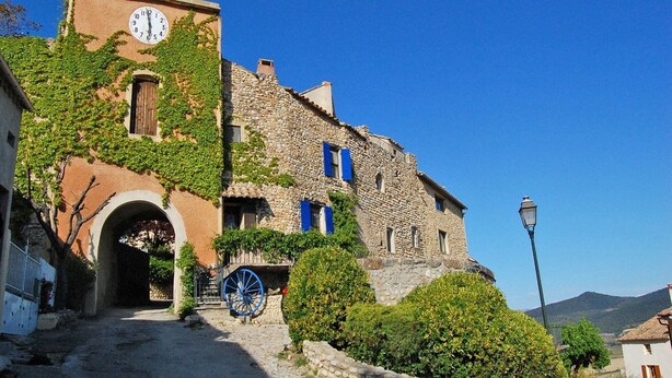 A historic stone building with a clock tower, an archway entrance, and a blue cart. - Holiday Home near Mont Ventoux Pool (Vaison-La-Romaine)