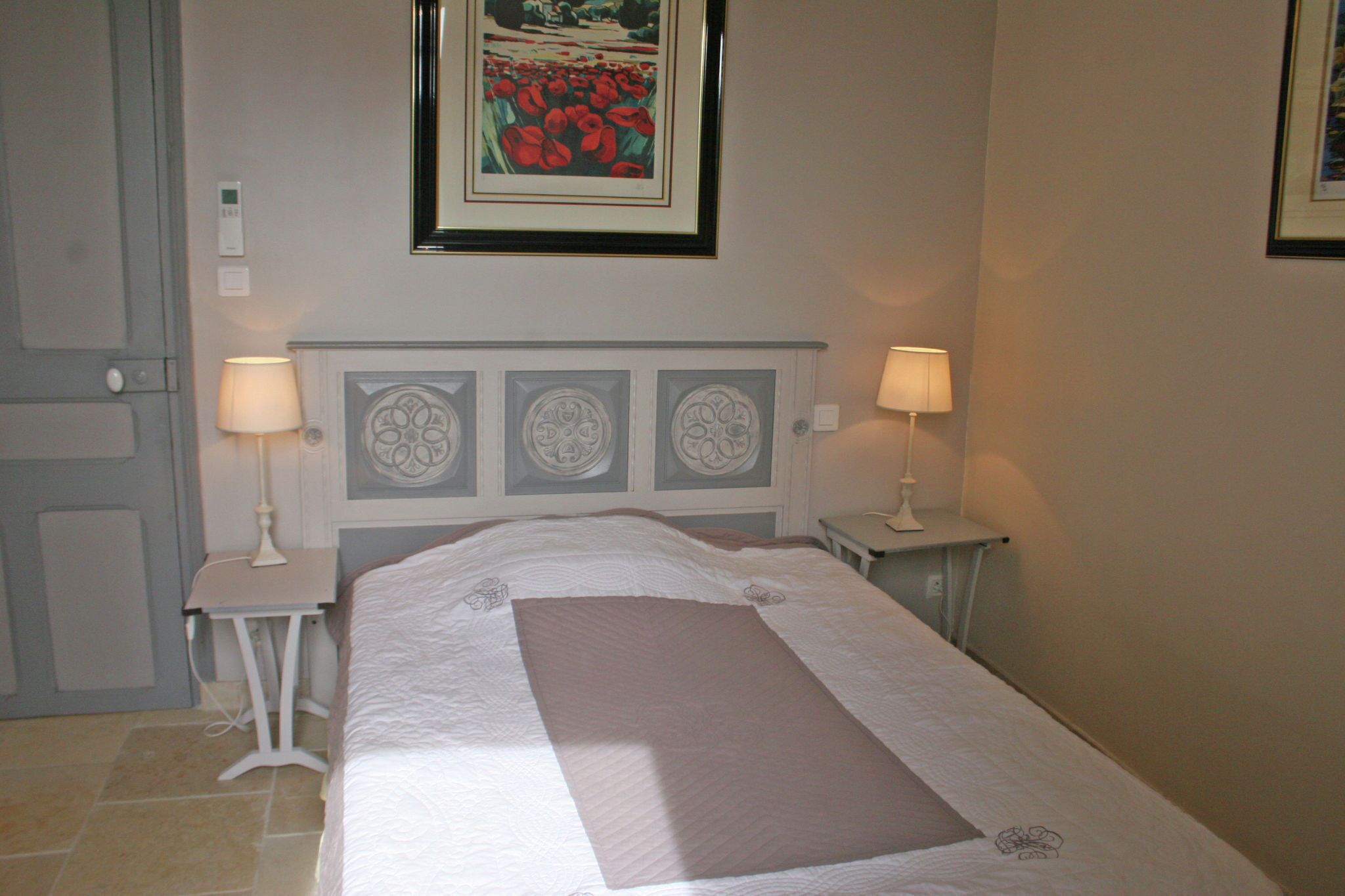 A neatly made bed with a decorative headboard, two bedside tables with lamps, and a framed artwork above the bed.