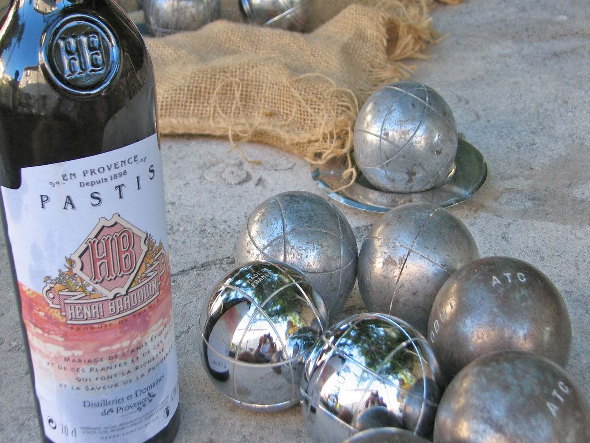 A bottle of Henri Bardou Pastis and several metallic spheres on a textured surface.