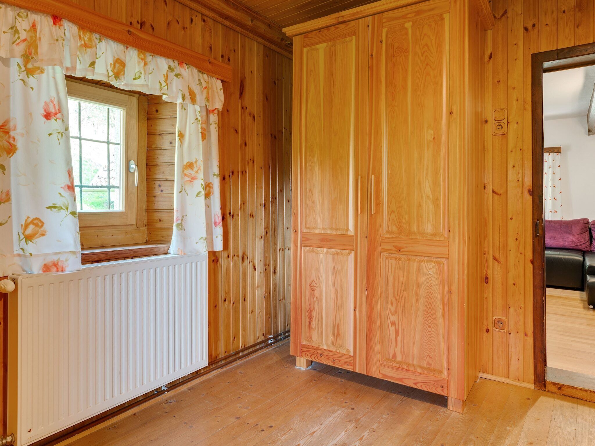 A wooden cabin interior with a window, a radiator, and a door.