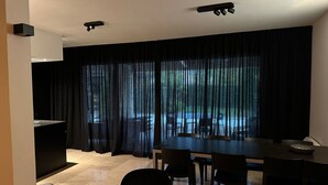 A modern dining area with a large table and chairs, a black curtain backdrop, and a view of the outdoors. - Villa in Malaucène with Private Pool (Malaucène)