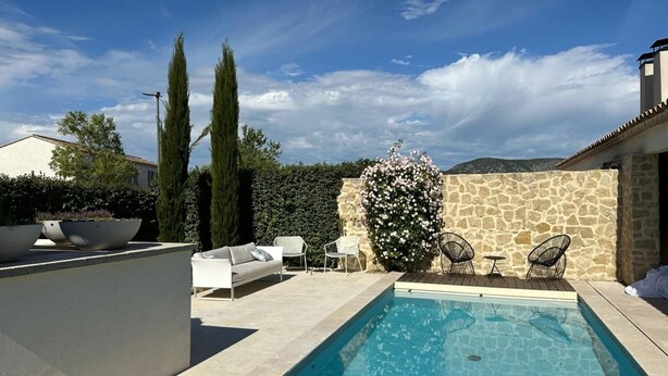 A swimming pool with a stone wall and a white fence, surrounded by outdoor furniture and a flowering bush. - Villa in Malaucène with Private Pool (Malaucène)