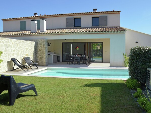 Une maison moderne dotée d’une piscine, d’un espace salon extérieur et d’un mur en pierre.