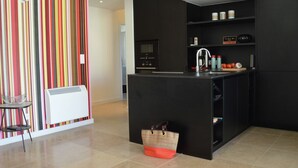 A modern kitchen with a black countertop, a built-in oven, and a sink. There is a striped wall and a small table with a chair. - Villa in Malaucène with Private Pool (Malaucène)