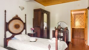 A bedroom with a wooden four-poster bed, a nightstand with a vase of flowers, a mirror, and a wardrobe.